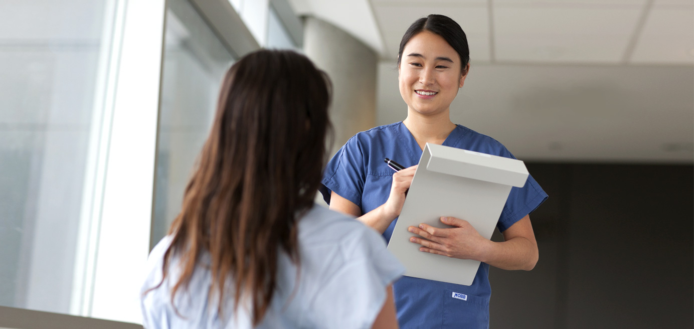 Nurse holding clipboard facing a patient sitting down