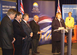 Debra McPherson at the podium with four males standing in a row to her right