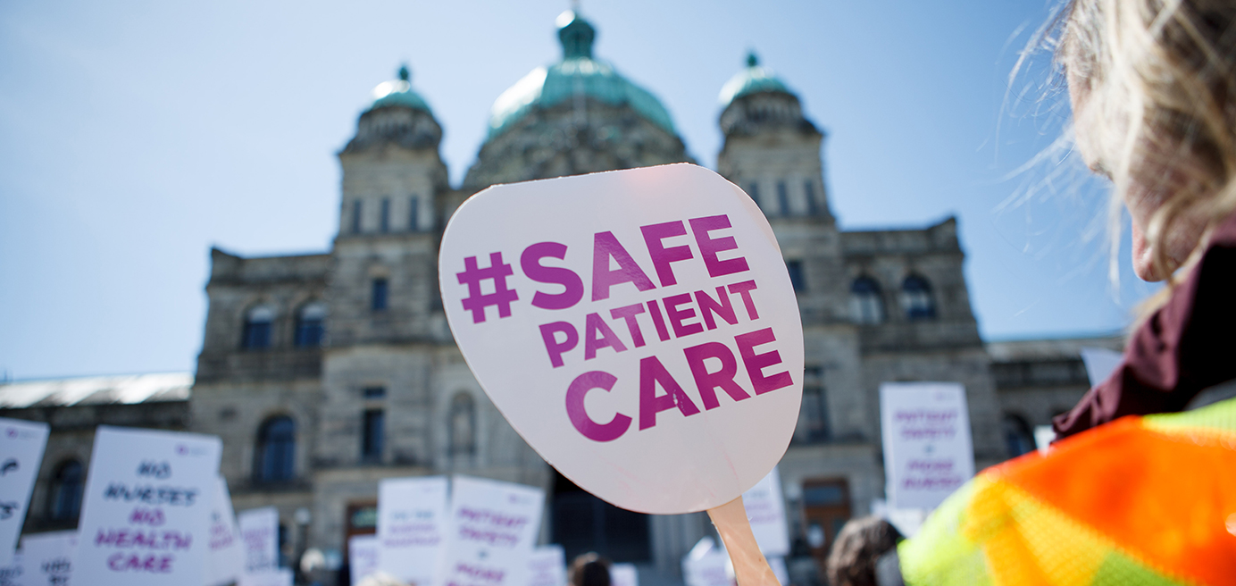 Person holding paddle with text, #Safe Patient Care, in front of parliament building
