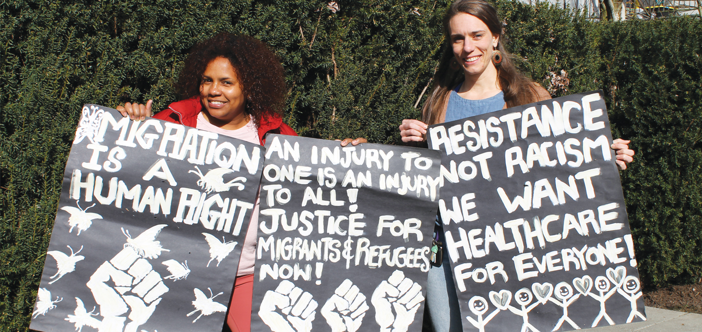 Photo of Sanctuary Health collective volunteers Maria Paralta and Natalie Blair holding signs