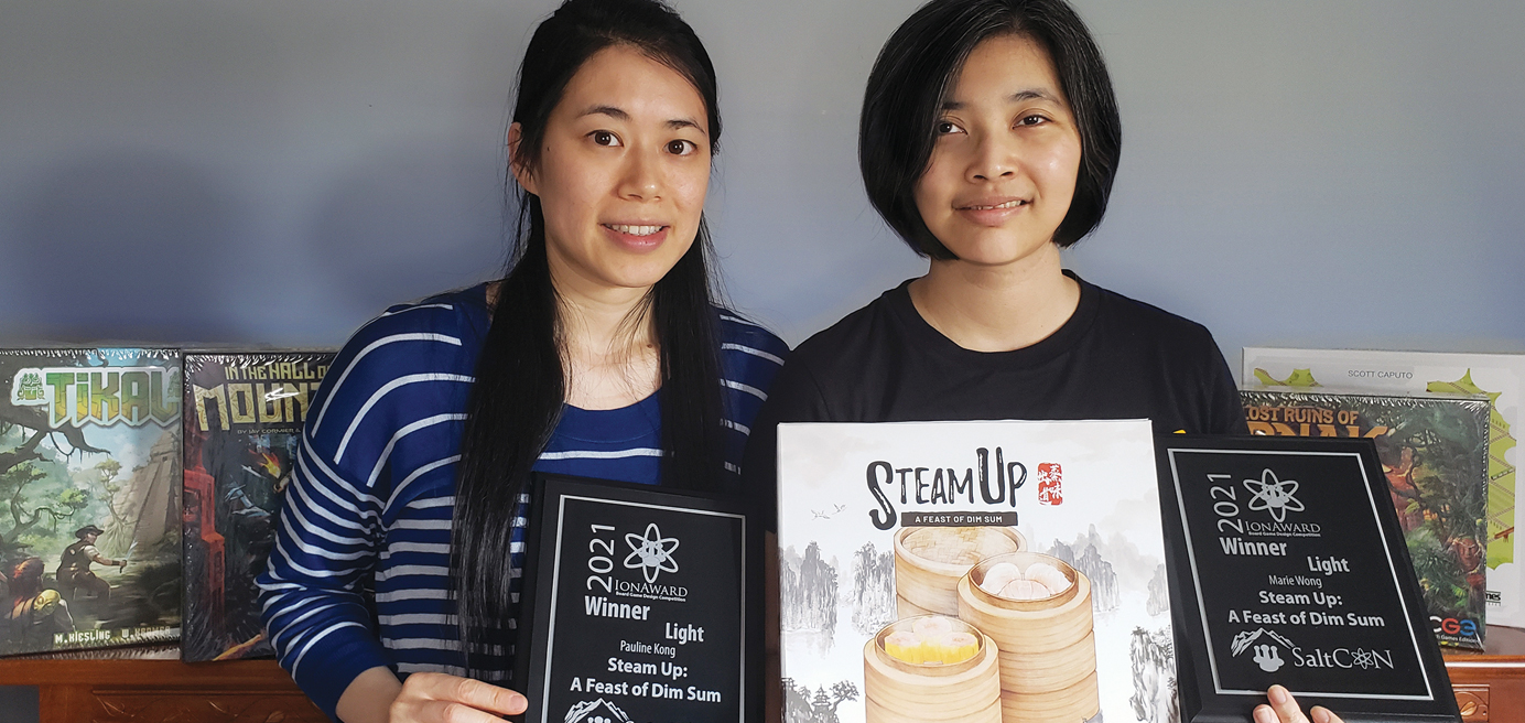 Photo of Pauline Kong and Marie Wong holding up the board game Steam Up: A Feast of Dim Sum