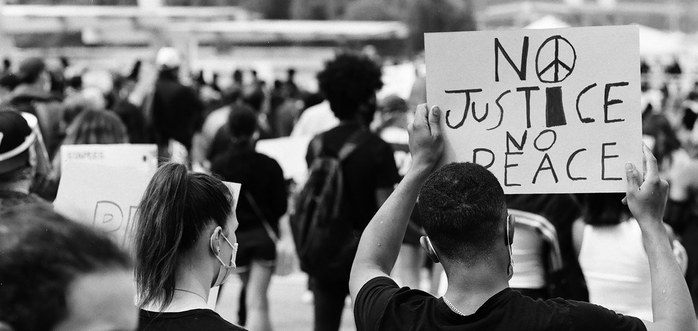 Person in a crowd holding 'No Justice No Peace' sign 