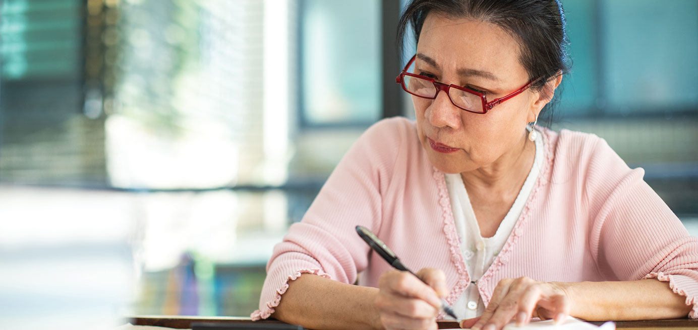 Asian woman sitting at table with pen and paper