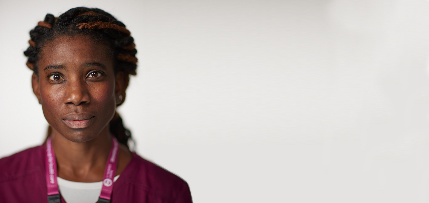 A black nurse facing the camera. She is on the left of the image with whitespace to the right of her.